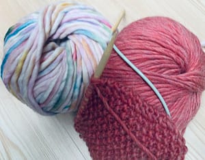 Zwei Wollknäuel mit Stricknadeln.