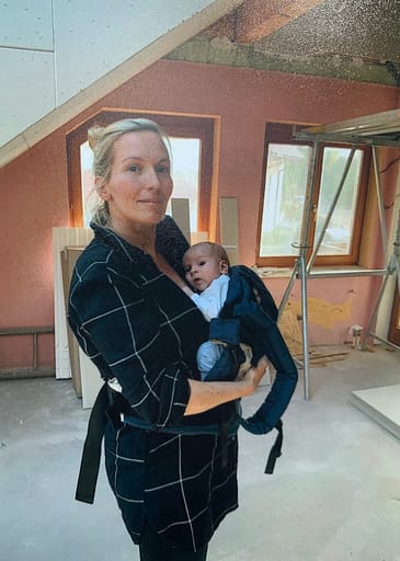 Eine Frau steht mit Baby auf dem Arm in einem Zimmer, das umgebaut wird.