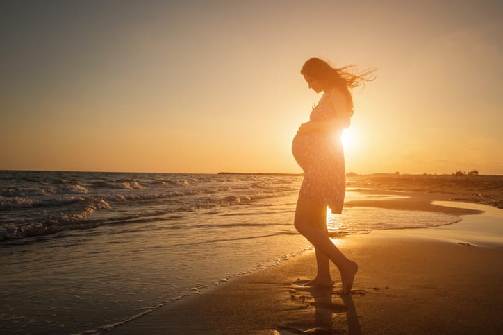 Schwangere Frau am Strand beim Sonnenuntergang.